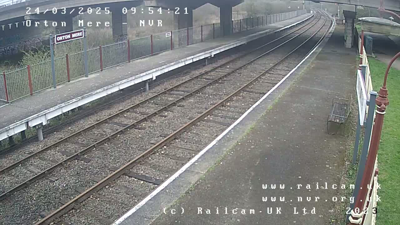 A mostly empty train platform with two train tracks under an overcast sky.