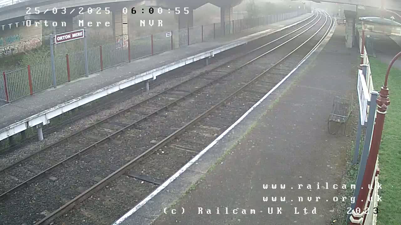 A foggy view of a train station platform with two sets of train tracks extending into the distance.