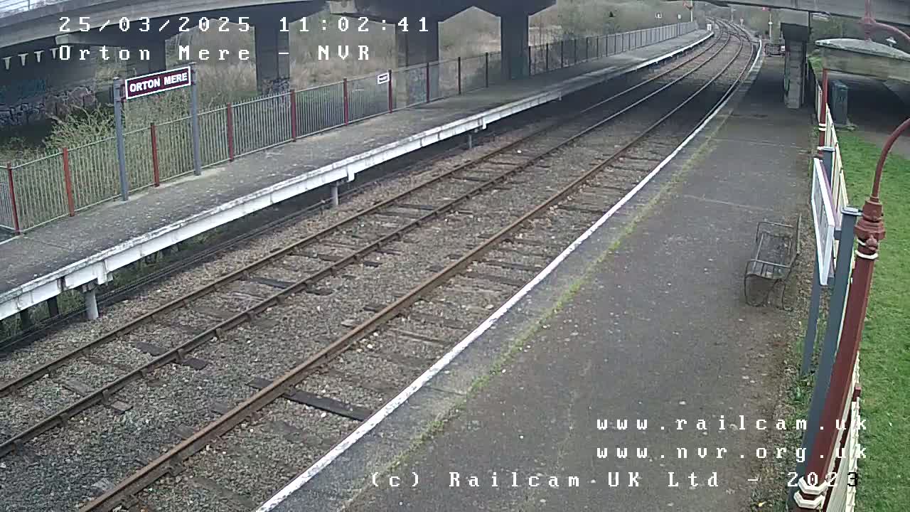 A mostly empty train platform with two sets of tracks under an overcast sky.