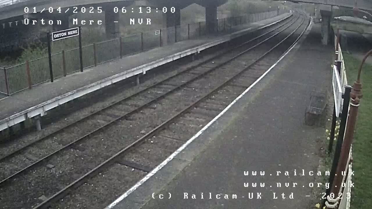 A train station platform with two train tracks under an overcast sky.