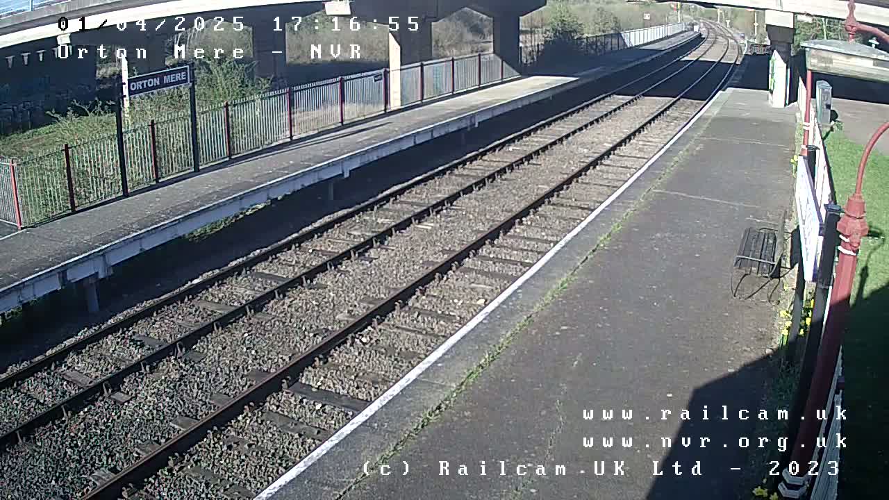 A sunny view of a train platform with two parallel train tracks extending into the distance.