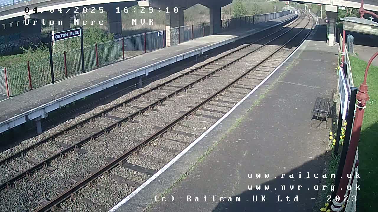 A mostly sunny view of a train station platform with a railway track extending into the distance.