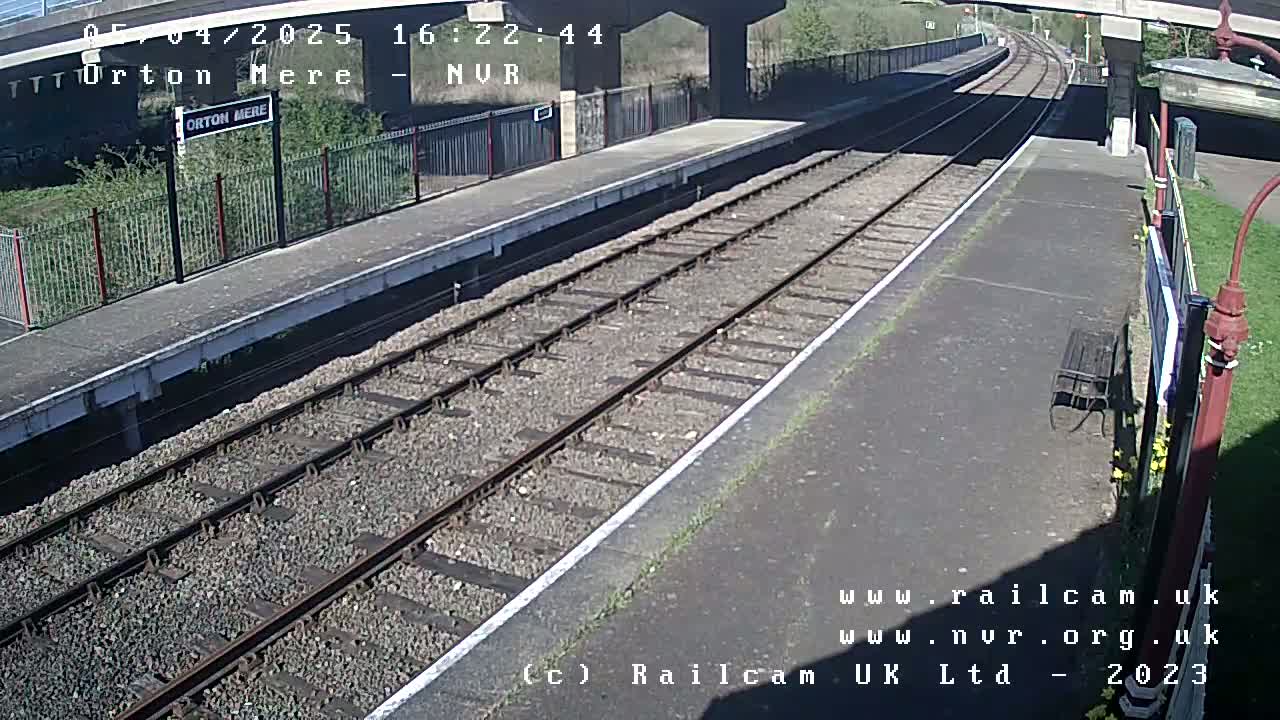 A mostly sunny view of a train station platform with two sets of train tracks extending into the distance.