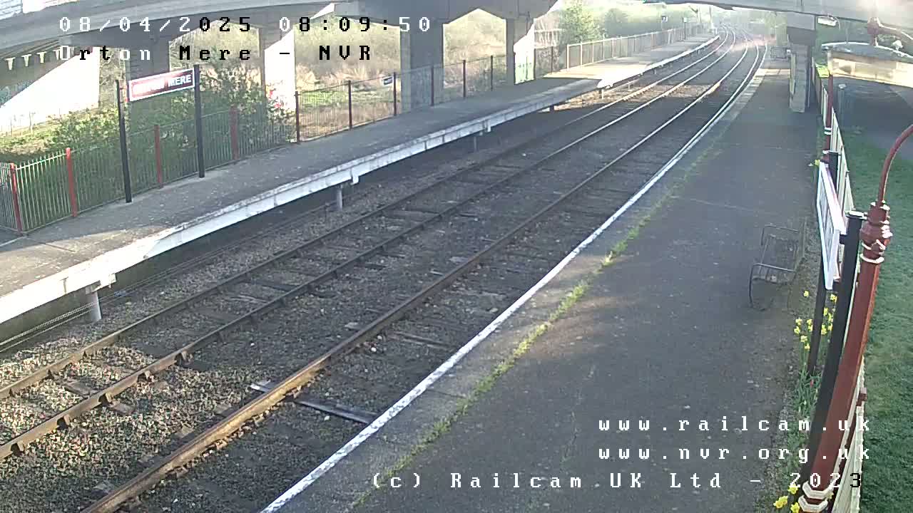 A sunny view of a train platform with two sets of train tracks extending into the distance.
