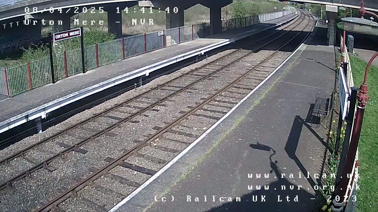 A sunny view of a train platform with railway tracks extending into the distance under a bridge.