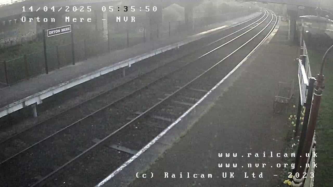 A foggy view of a train station platform with multiple train tracks curving away into the distance.