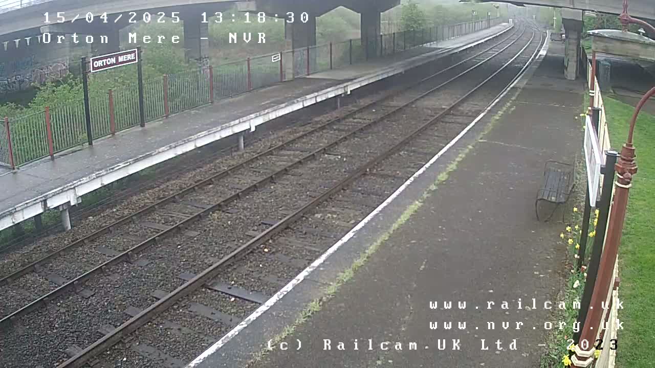 A view of a train station platform on an overcast day, showing train tracks extending into the distance.