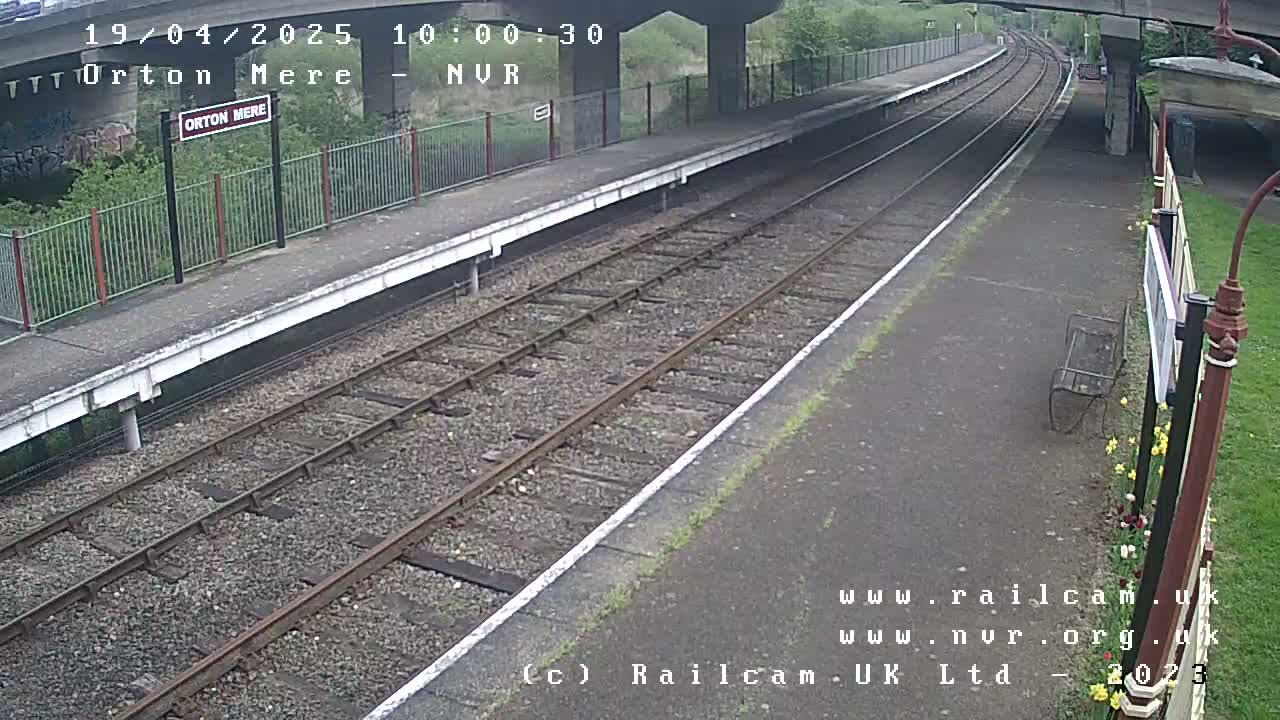 A train platform with railway tracks stretches into the distance under an overcast sky.