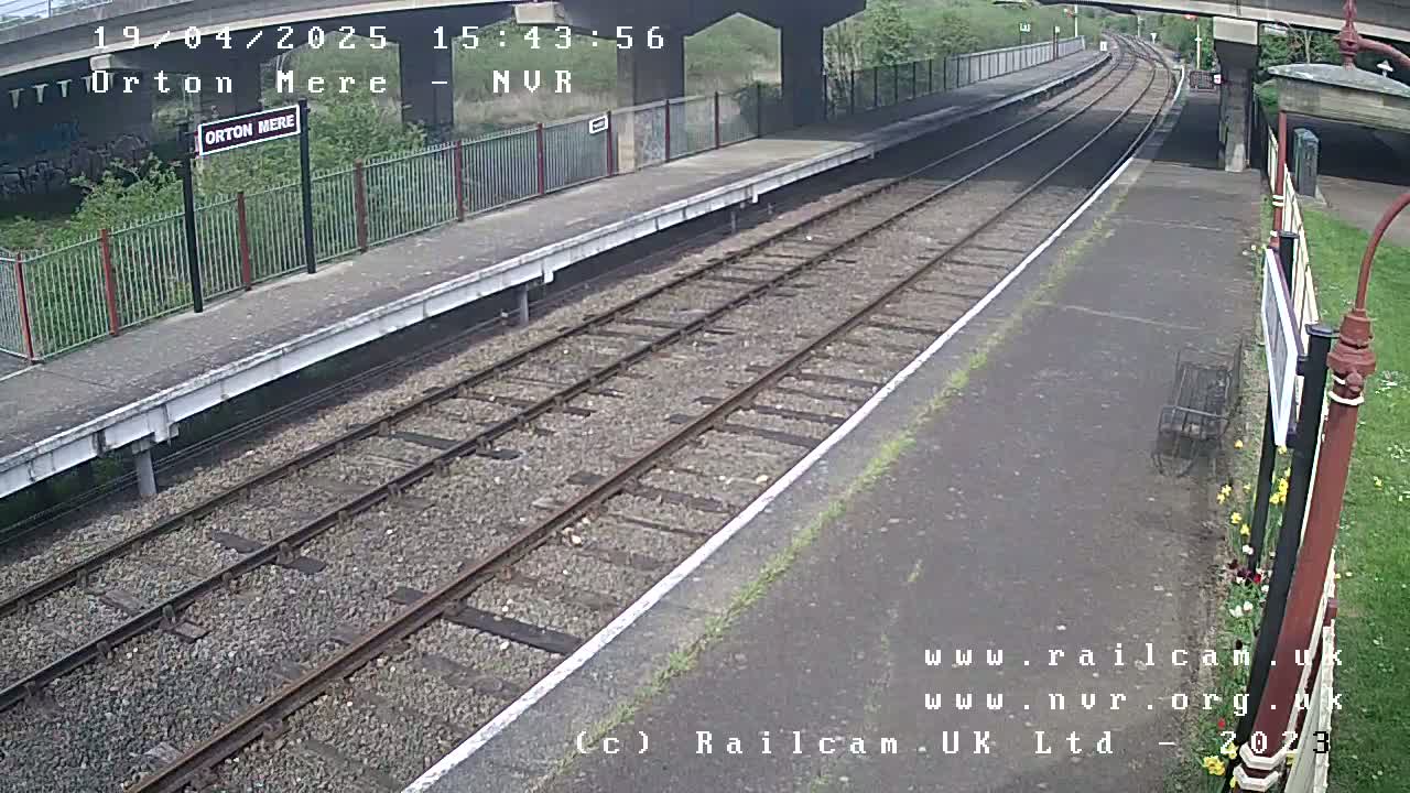 A train station platform with two parallel train tracks under a partly sunny sky.