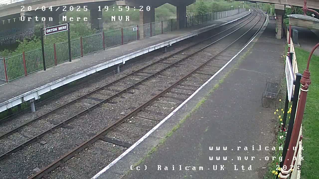 A train station platform with two sets of train tracks under an overcast sky.