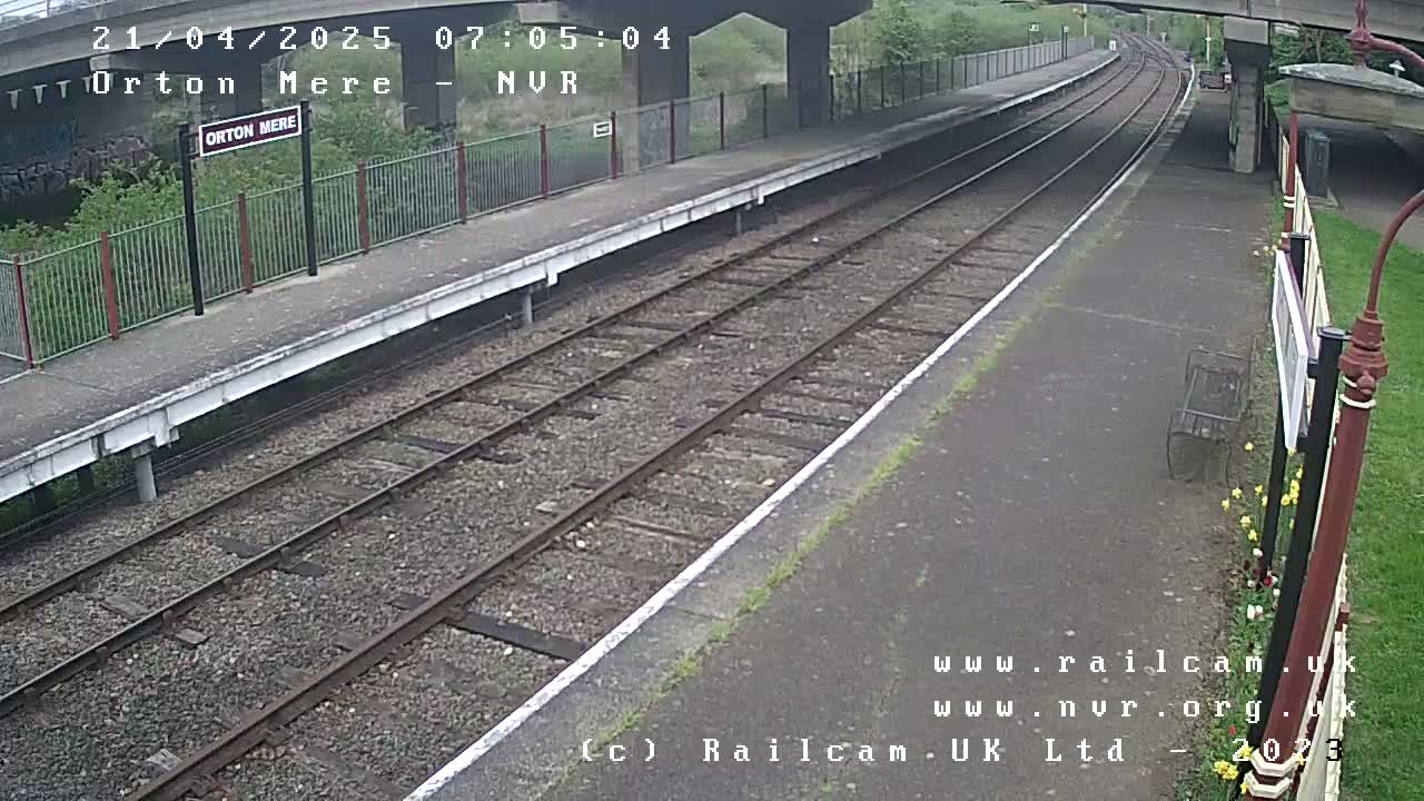 A mostly empty train station platform with two sets of train tracks under an overcast sky.