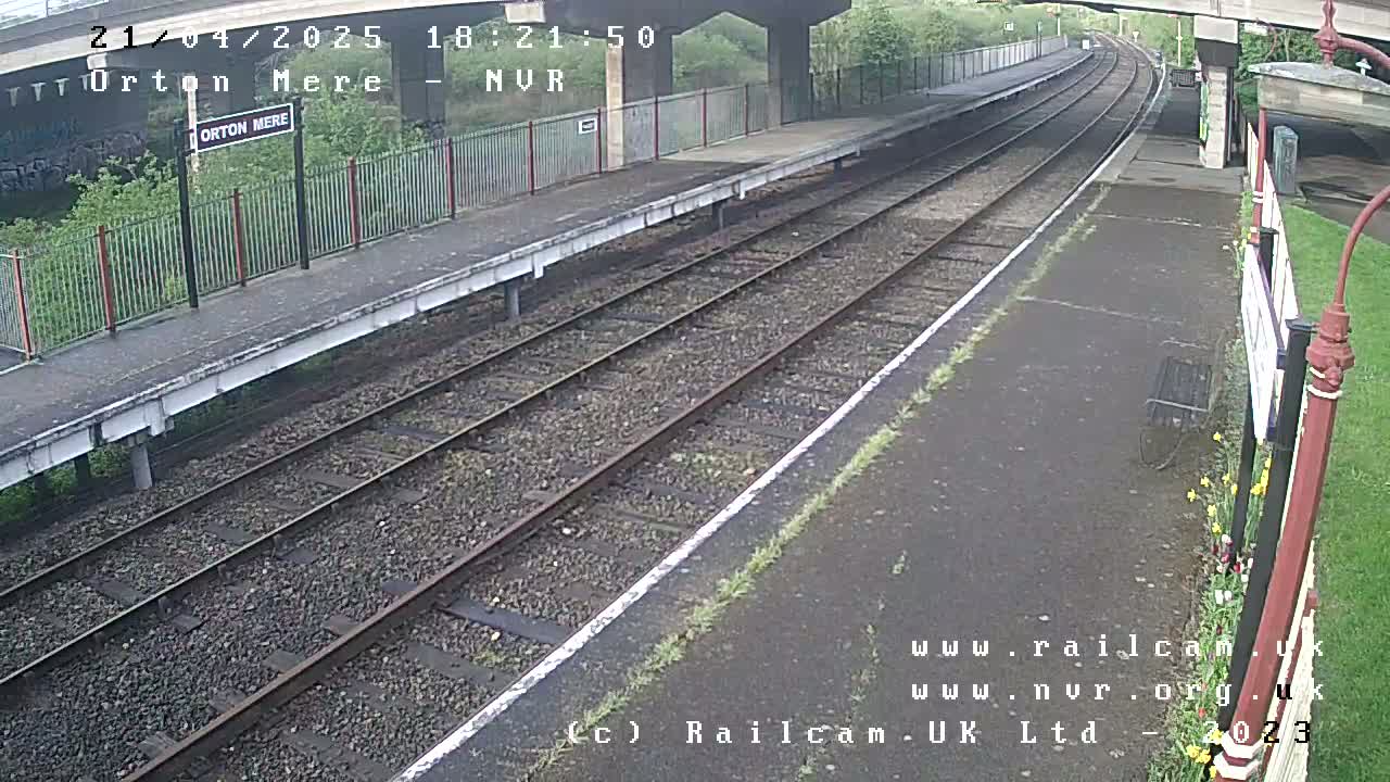 A train platform with two railway tracks stretches into the distance under an overcast sky.