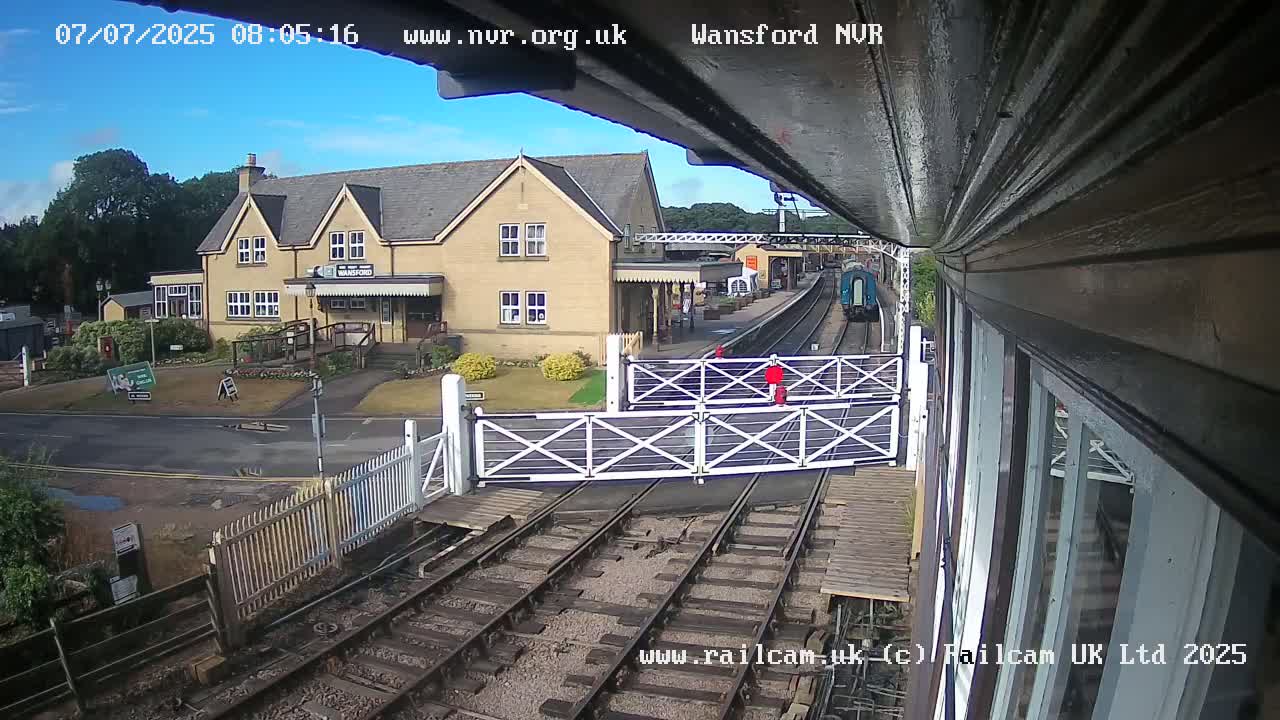 A train passes through a level crossing at a railway station on a sunny day.