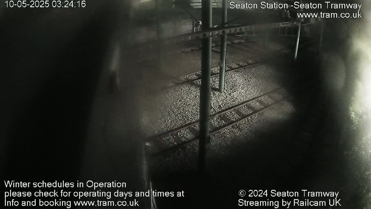 A nighttime, high-angle view shows empty train tracks covered in light-colored gravel.