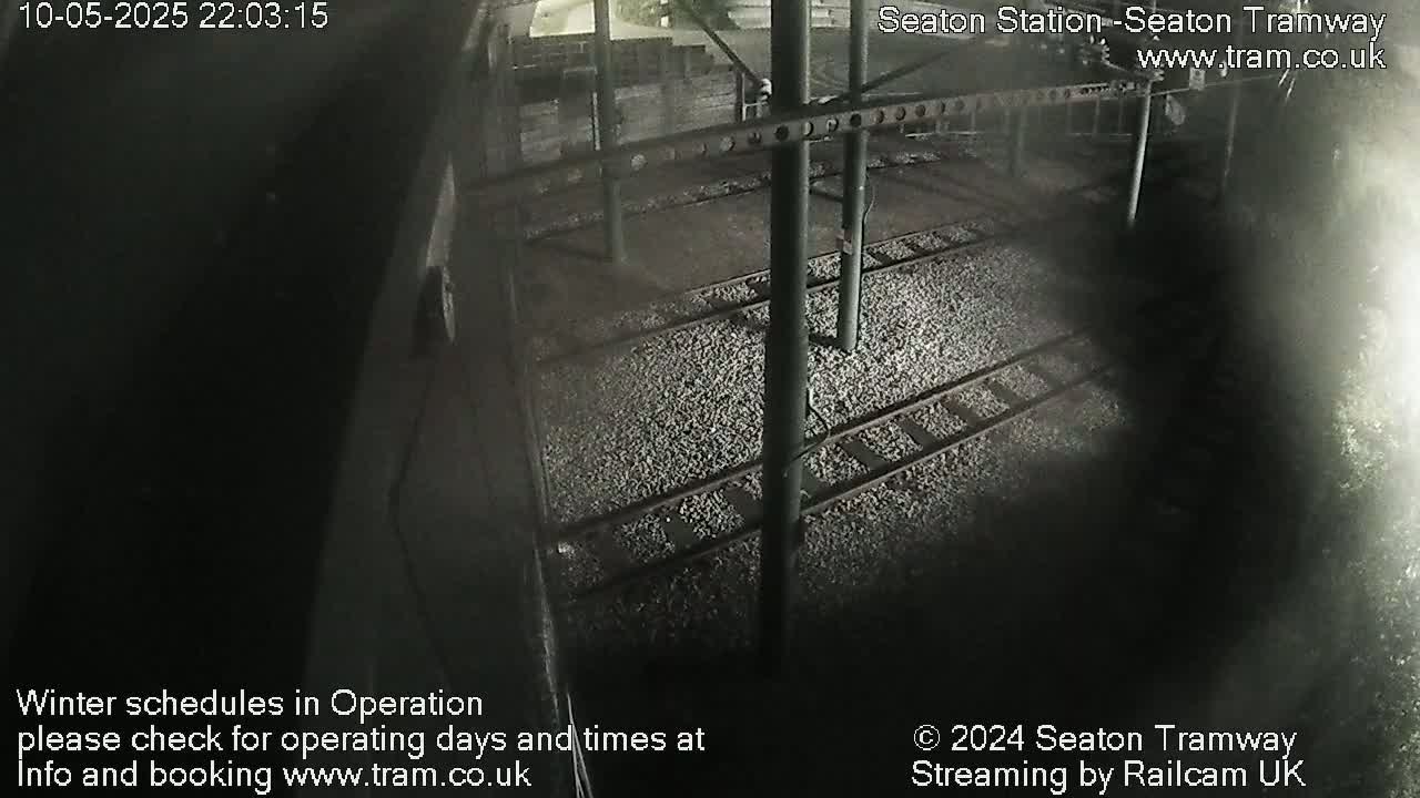 A nighttime, dimly lit view of train tracks covered in gravel, beneath a metal structure.