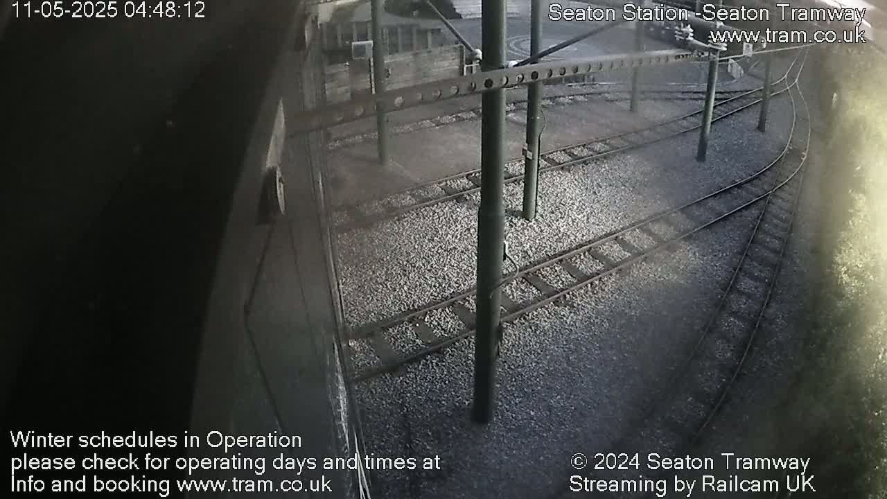 A high-angle, outdoor view shows several train tracks diverging from each other on a gravel surface under dark, overcast conditions.