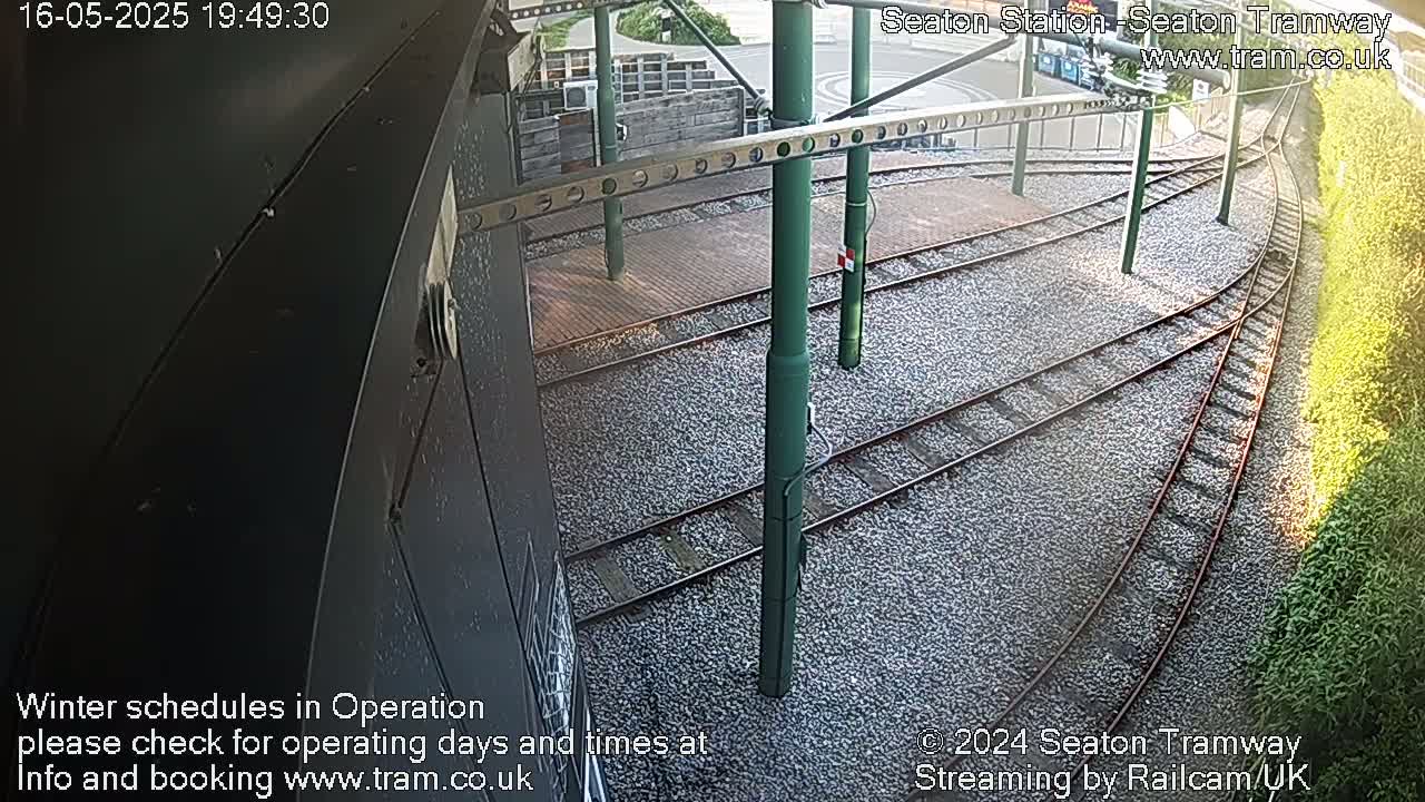 A high-angle view shows a railway track junction at a tram station on a sunny day.