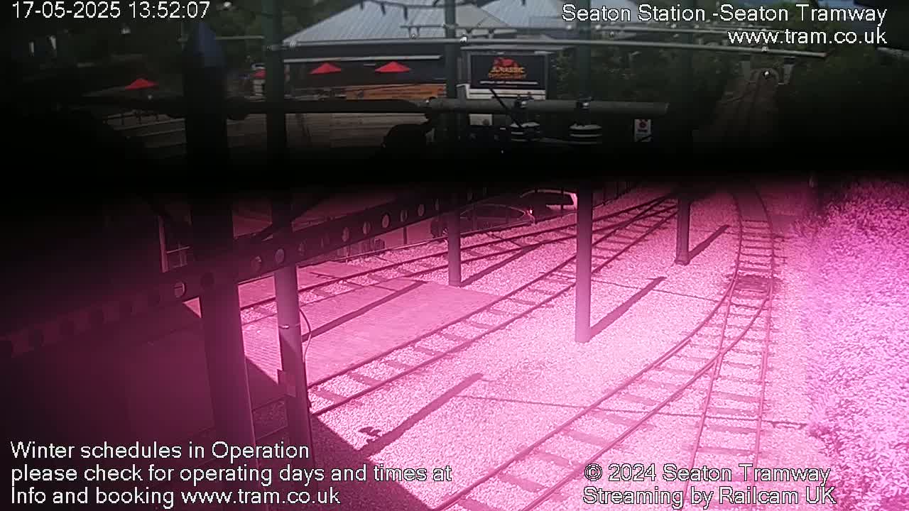 A high-angle view shows a section of railway tracks curving slightly, set within a gravel surface, partially shaded by overhead structures.