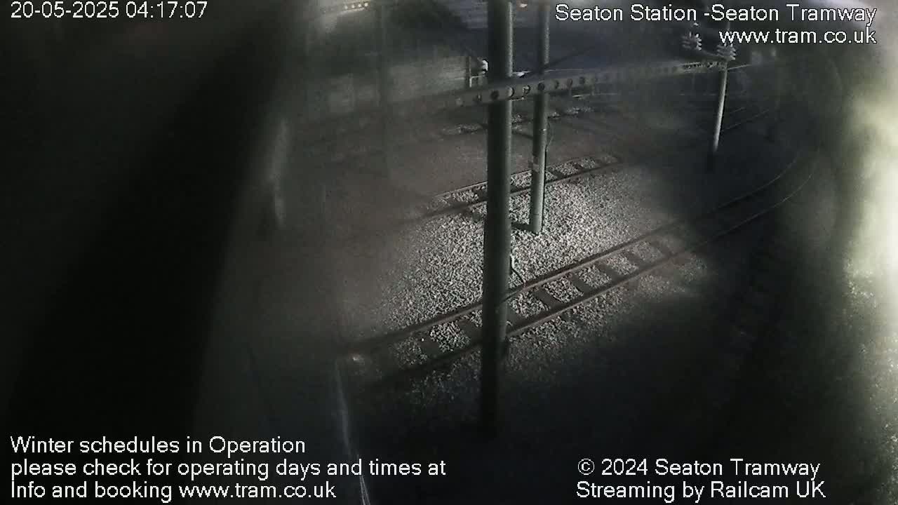 A nighttime, dimly lit view of train tracks and overhead electrical equipment at a station.