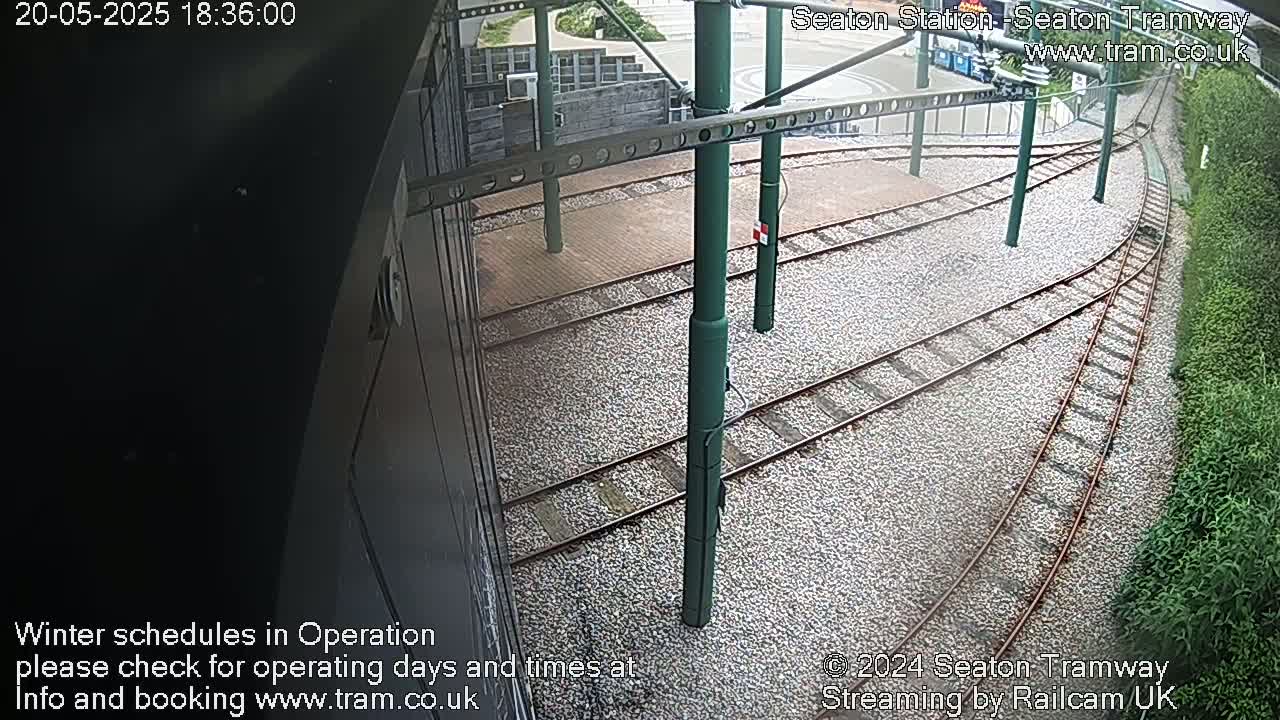 A high-angle view of tram tracks and supporting infrastructure at a station, bordered by vegetation.