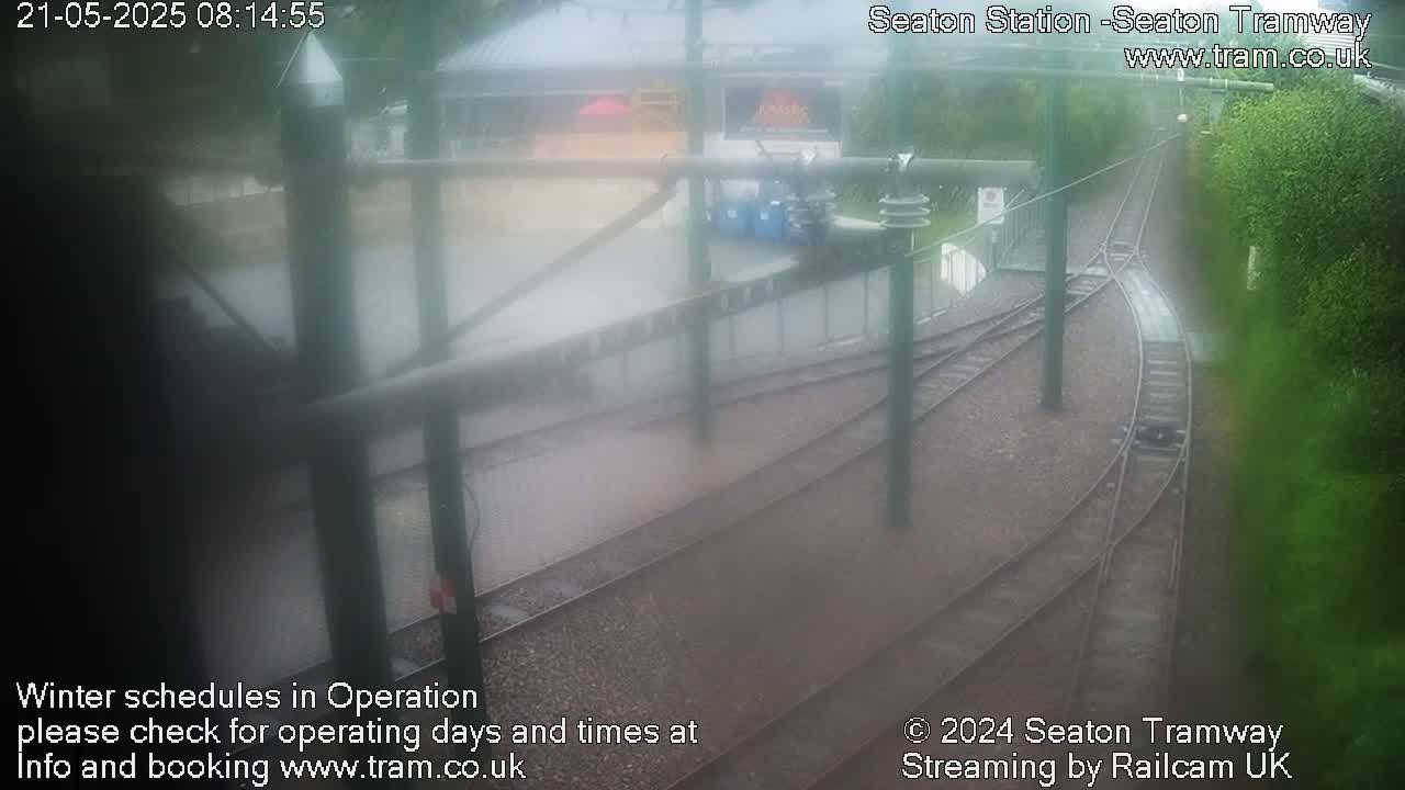 A rain-slicked tram station with several sets of tracks branching off, viewed from an elevated position.