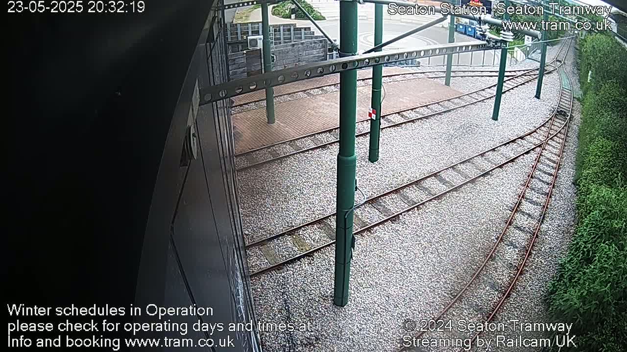 An overhead view shows a tram station's track layout, with converging tracks set on a gravel bed next to green shrubbery.