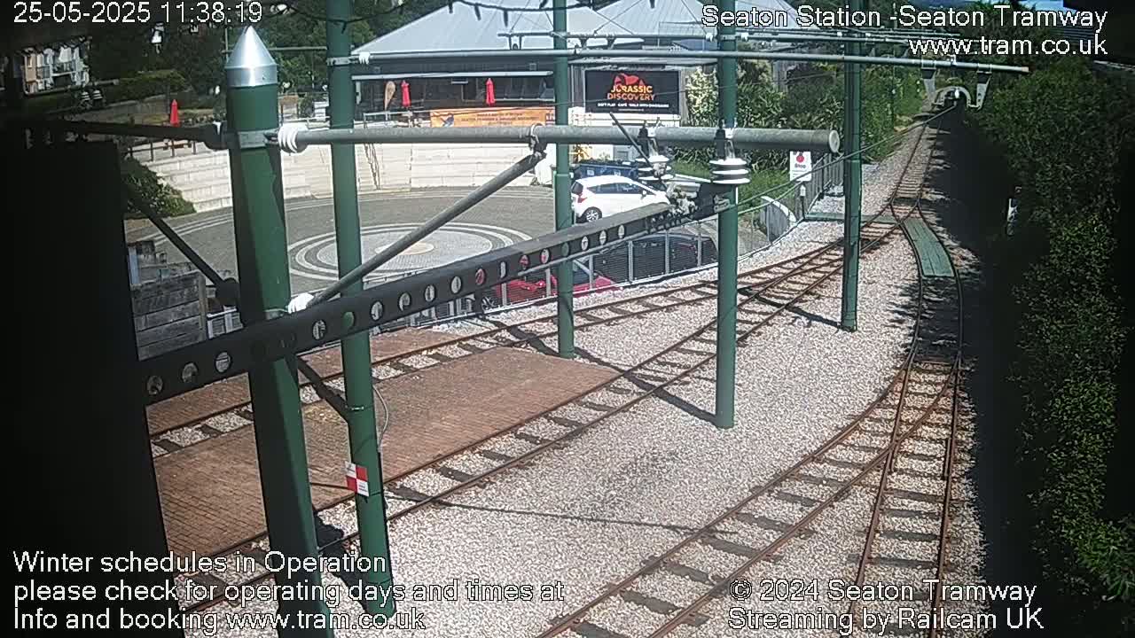 A sunny overhead view of train tracks curving through a station area next to a building and some greenery.