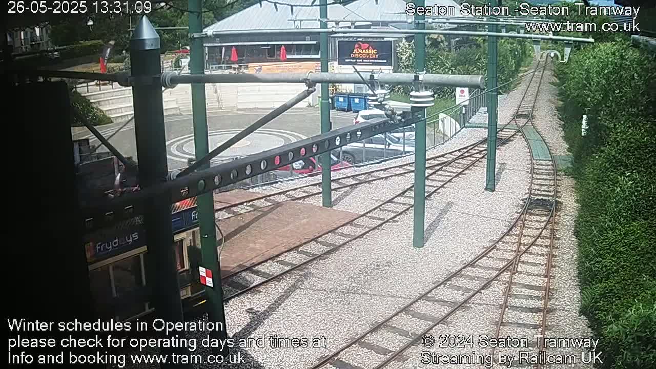 A tram is stopped at a station, which has a curving track leading away from it, under a partly sunny sky.