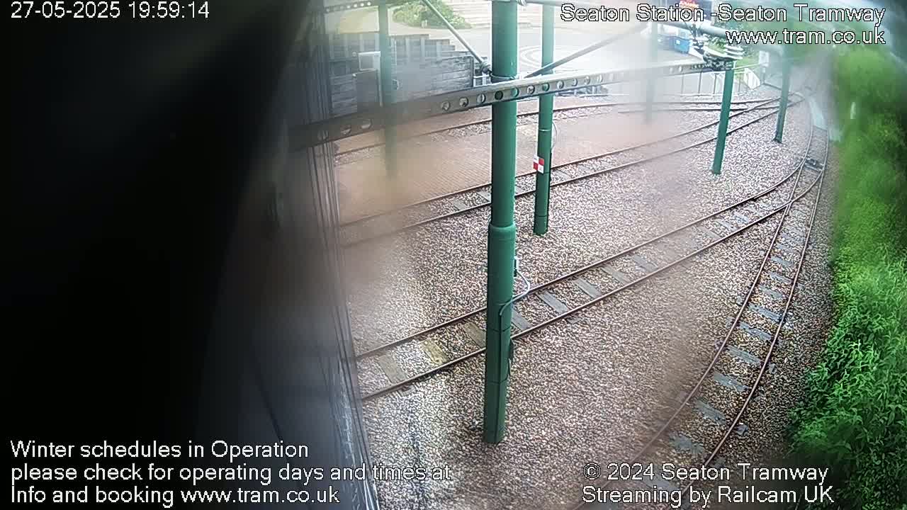 A rainy view of tram tracks curving to the right, bordered by green vegetation.