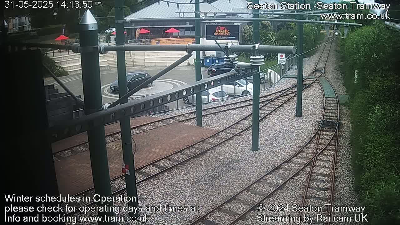 Tram tracks curve through a station area with several cars parked nearby, under partly cloudy skies.
