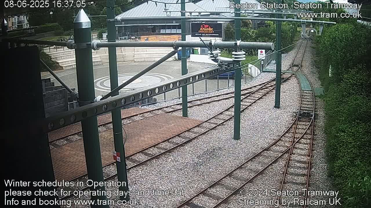 A high-angle view of tram tracks curving around a paved area next to a building and lush greenery.
