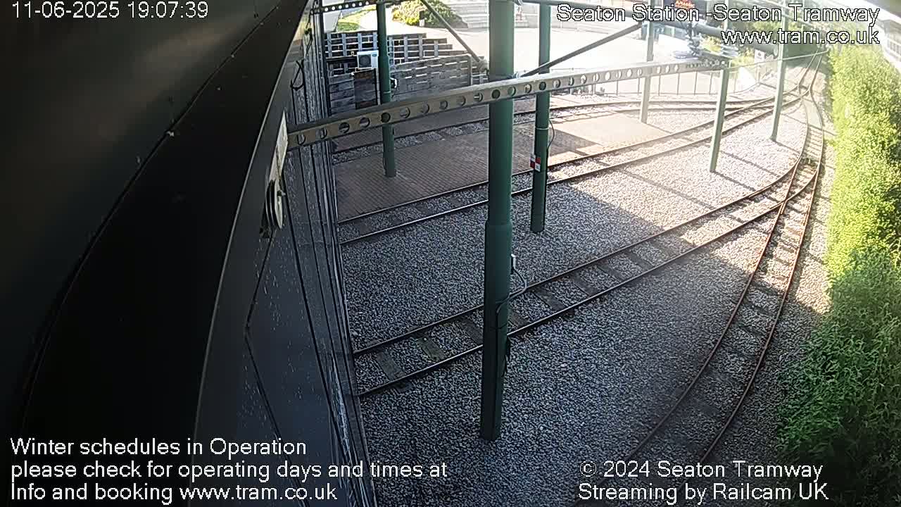 Tram tracks curve gently through a gravel-covered area next to a low hedge in the sunlight.