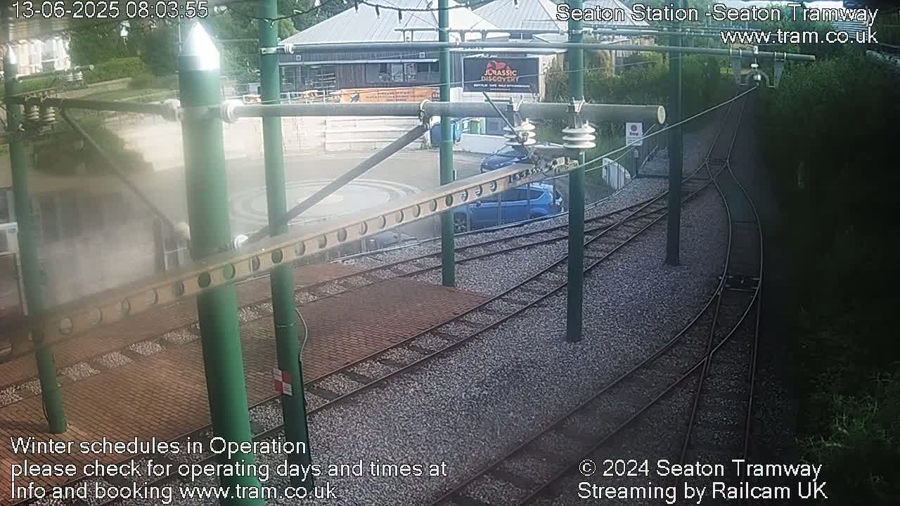 A blue car is parked near a tram station's turning loop on a partly cloudy day.