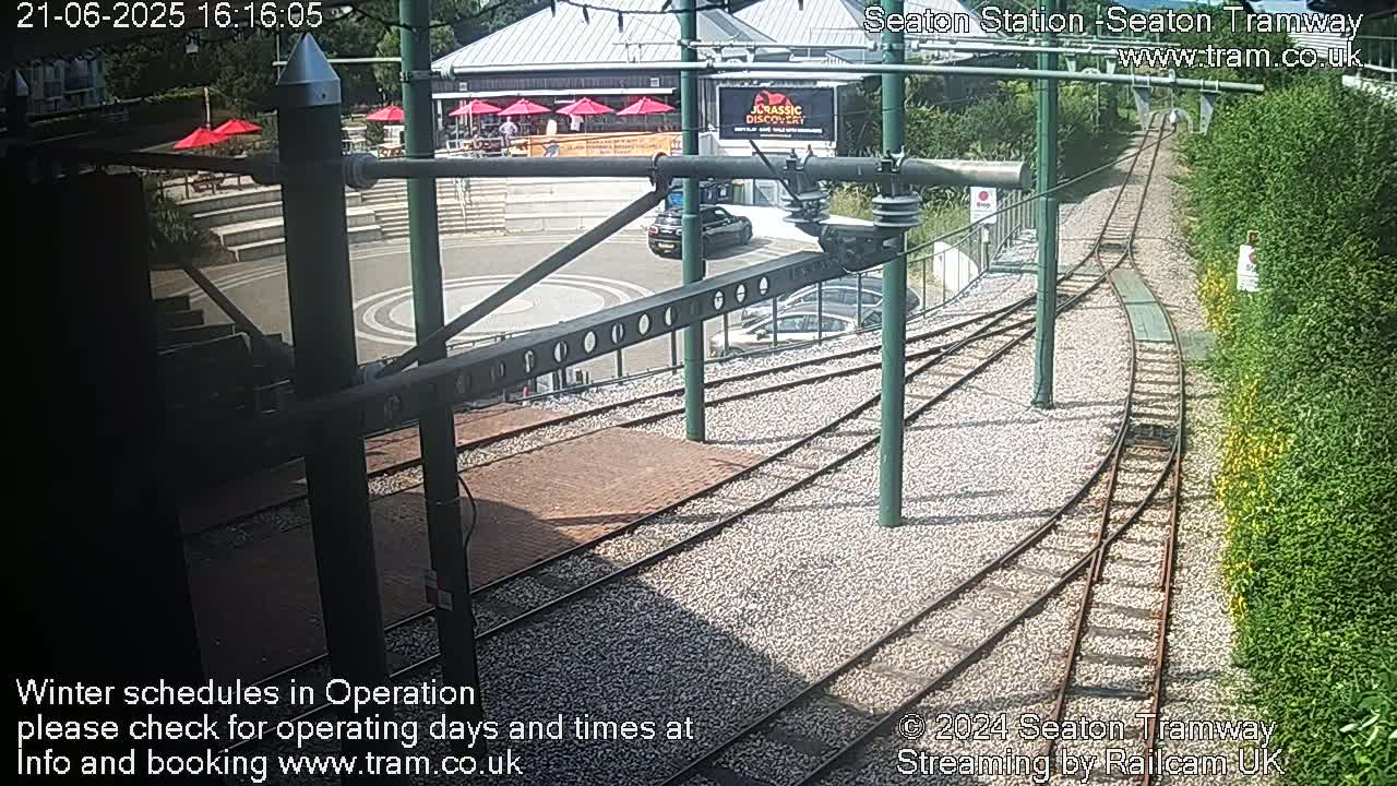 Tram tracks curve alongside a building and a landscaped area on a sunny day.