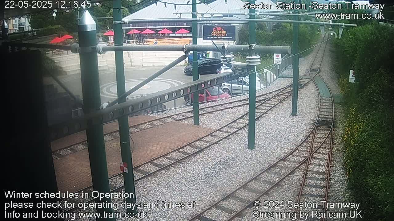 Tram tracks curve through a station area with several cars parked nearby, under an overcast sky.