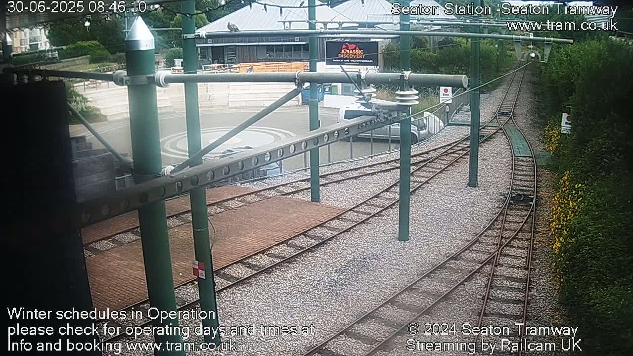 A tram station with a turning loop and tracks, partially surrounded by greenery, on an overcast day.