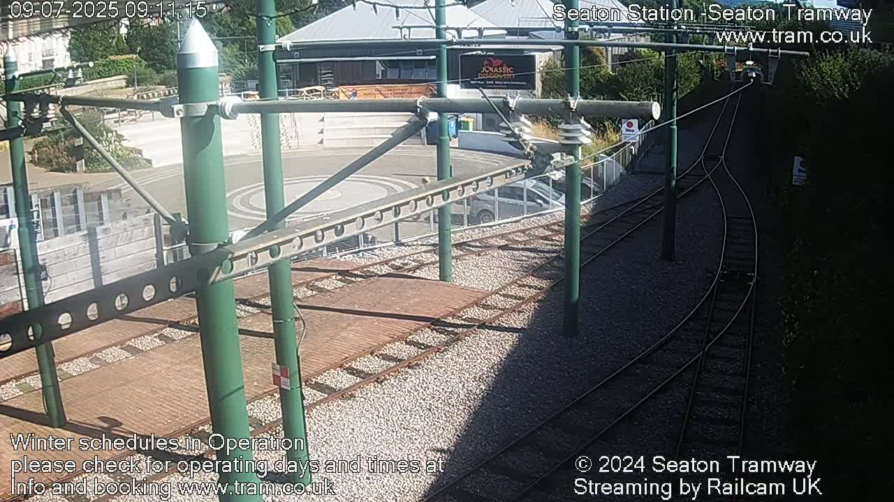 A sunny overhead view of a tram station with train tracks and a building in the background.