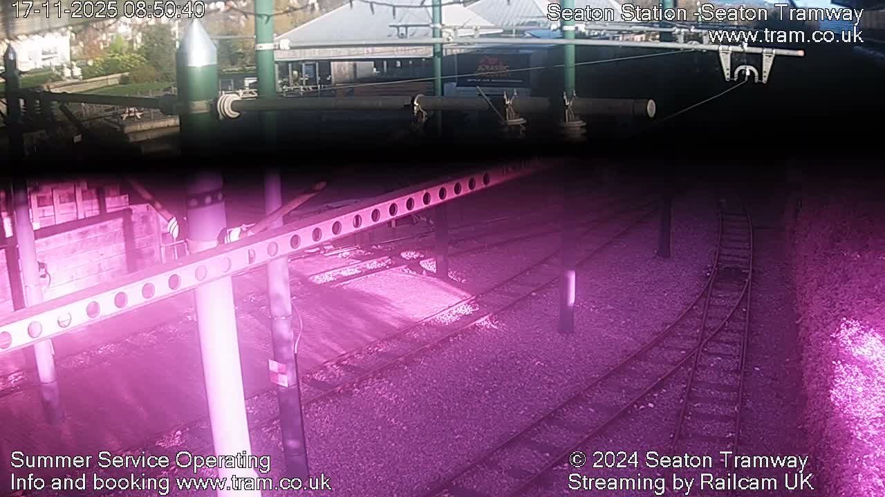 The image shows a split view, with the upper half depicting an outdoor daytime scene of a tramway station with overhead lines and buildings under clear skies, while the lower half presents tram tracks and gravel illuminated by a prominent pink and purple glow.