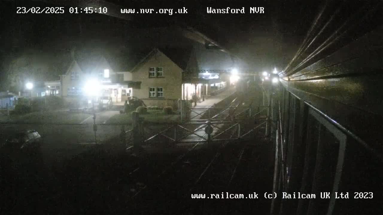 A nighttime view from a train shows a small station building and a closed gate, under foggy or misty conditions.