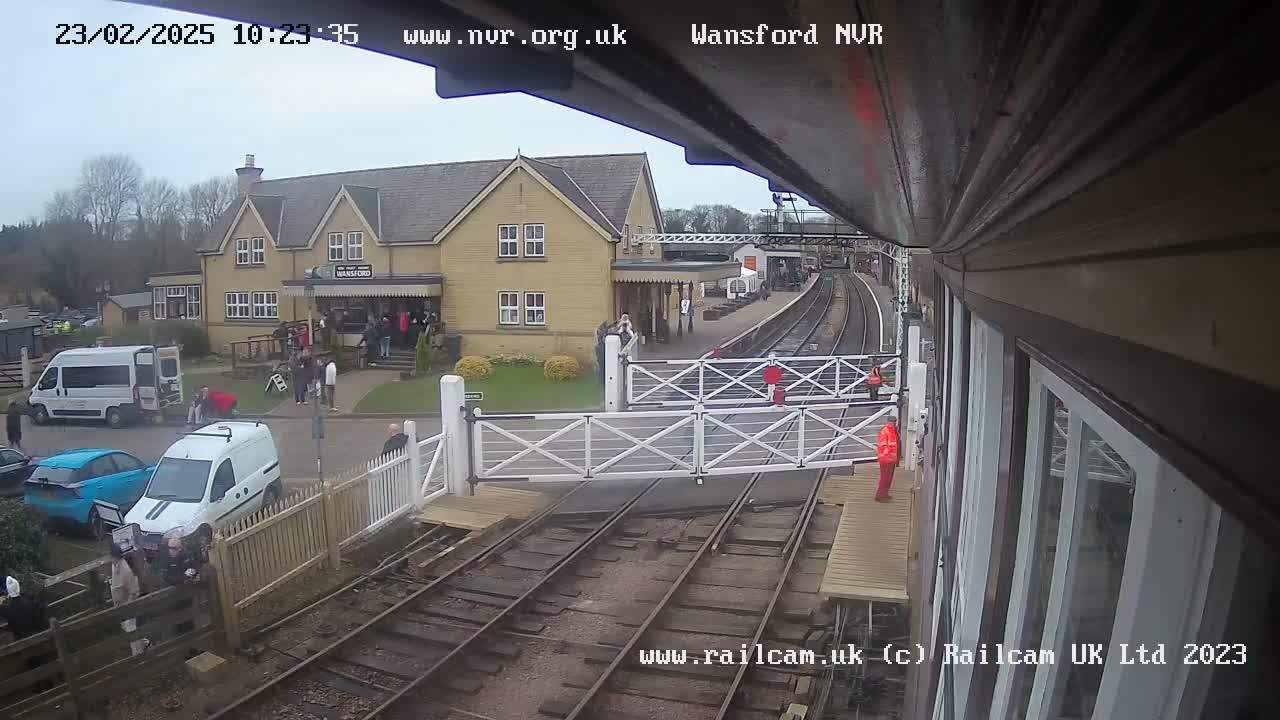 A train station with a two-story building and several people gathered outside under an overcast sky.