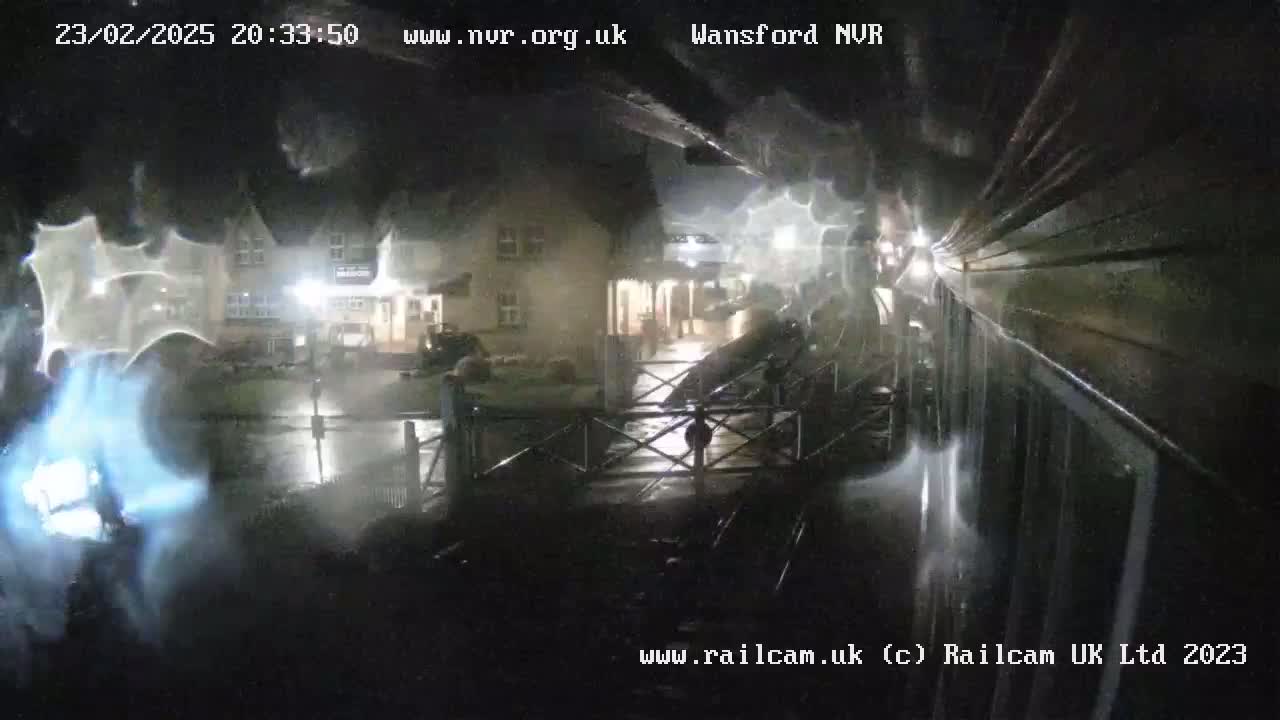 A nighttime, rainy view of a wet, empty street in front of a building, seen through a rain-streaked window.