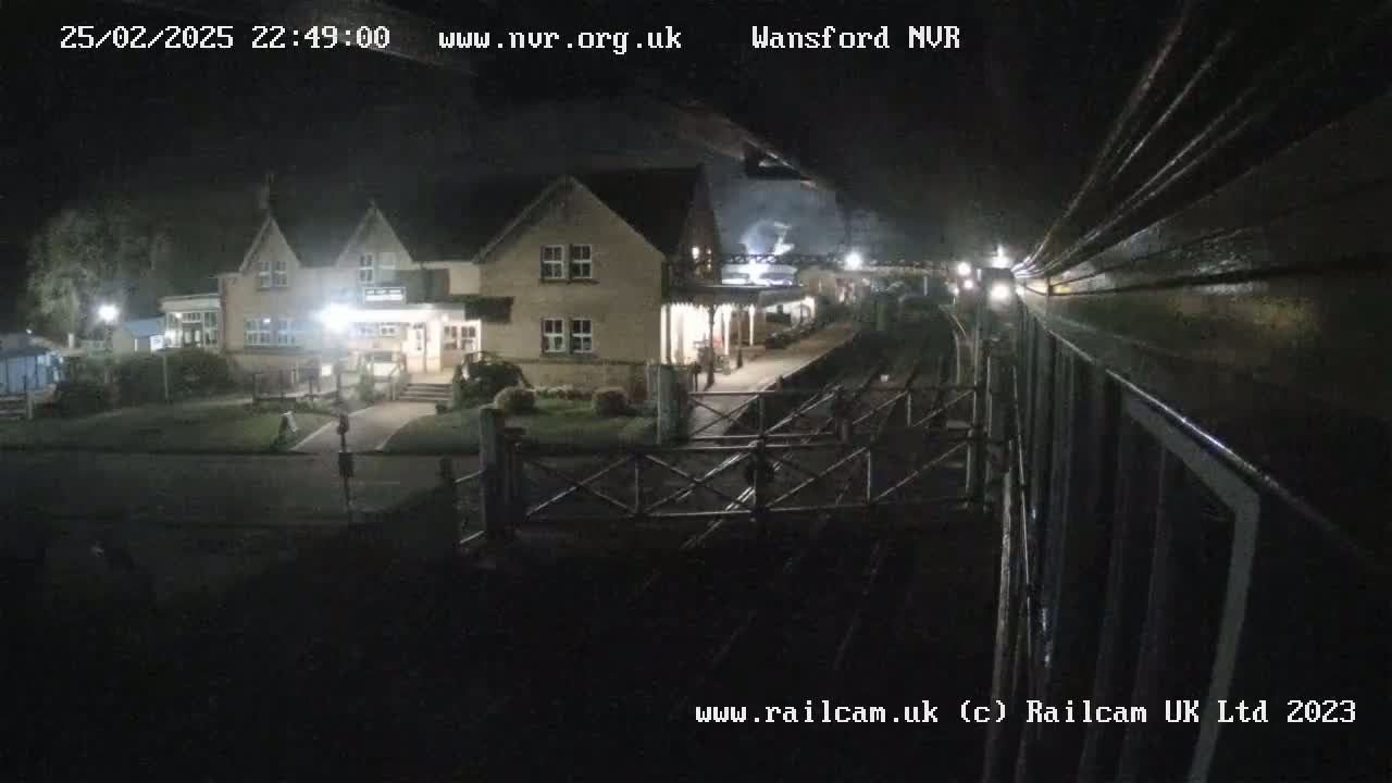A nighttime view from a train shows a building with lights on near a railway crossing.