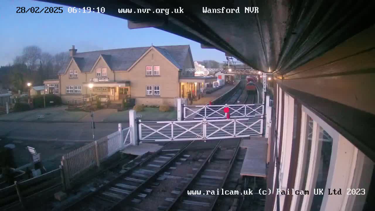 A train passes a station building under a clear, pre-dawn sky.