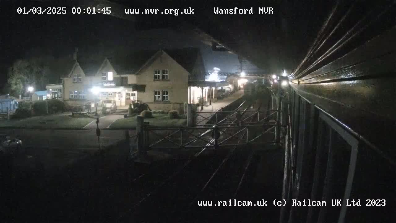 A nighttime view from a train shows a railway station with a building and a crossing gate.