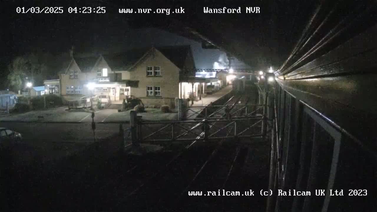 A nighttime view of a train station, featuring a two-story building and a covered platform area.
