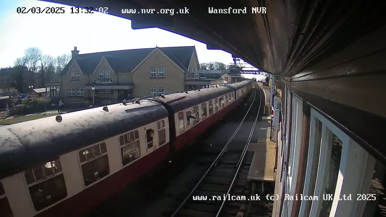 A long, red and black passenger train is departing a station on a sunny day.