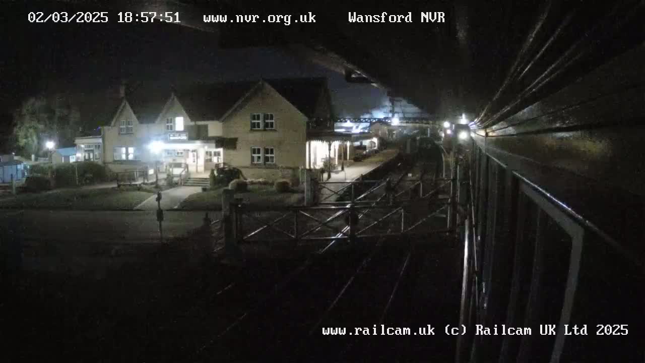 A nighttime view from a train shows a two-story building and a train station platform.