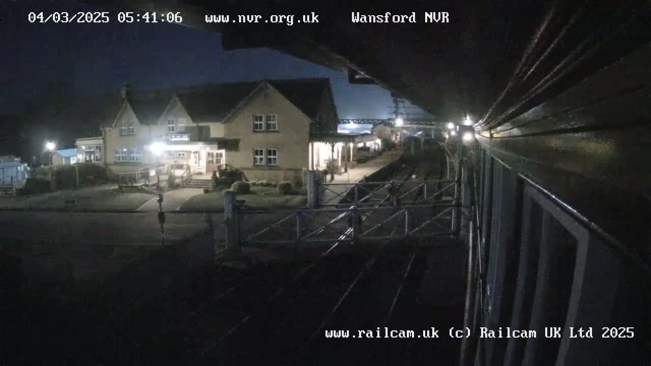 A nighttime view of a train station building and railway tracks under a dark sky.