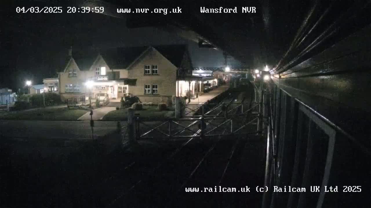 A nighttime view from a train shows a two-story building with lights on near a railway crossing.