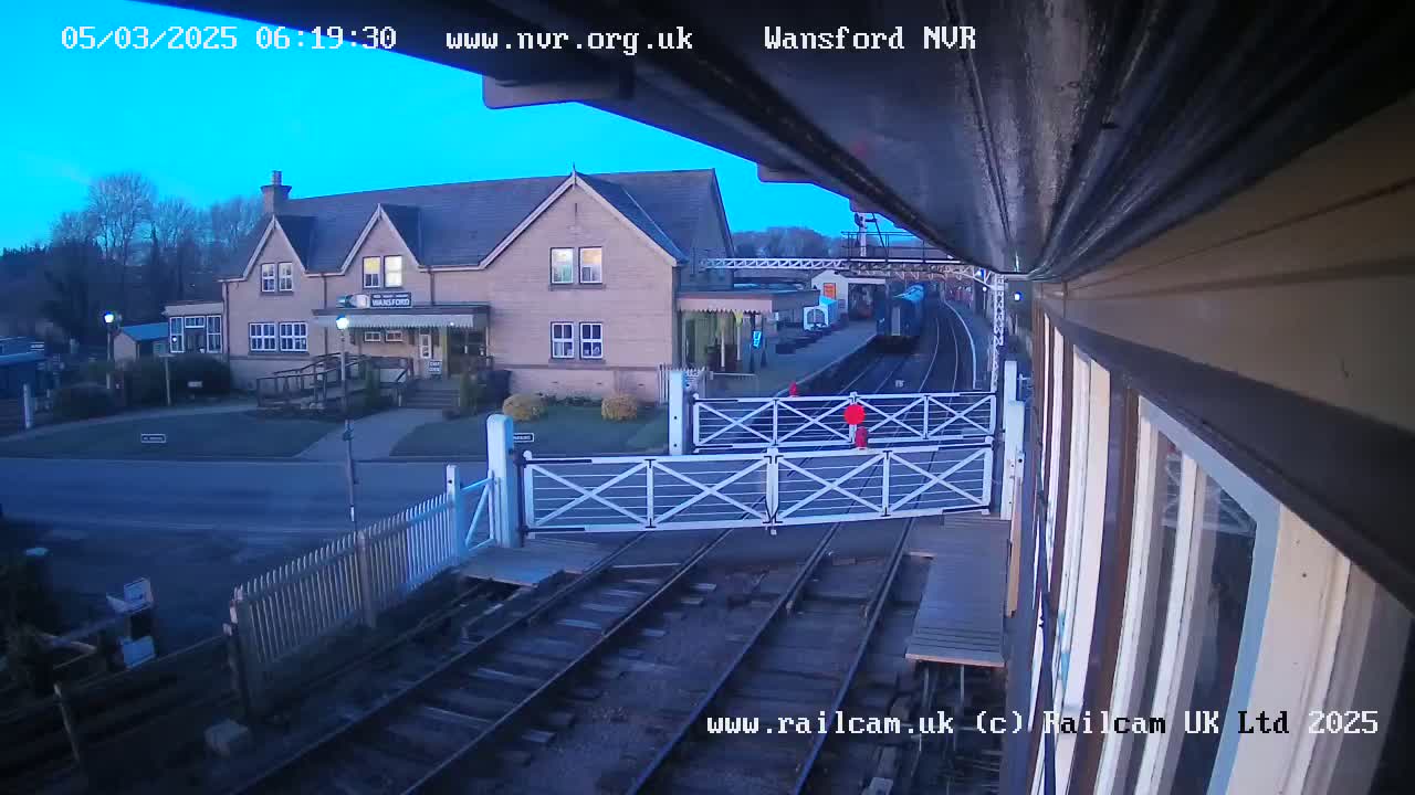 A train is departing a station near a building under a twilight sky.